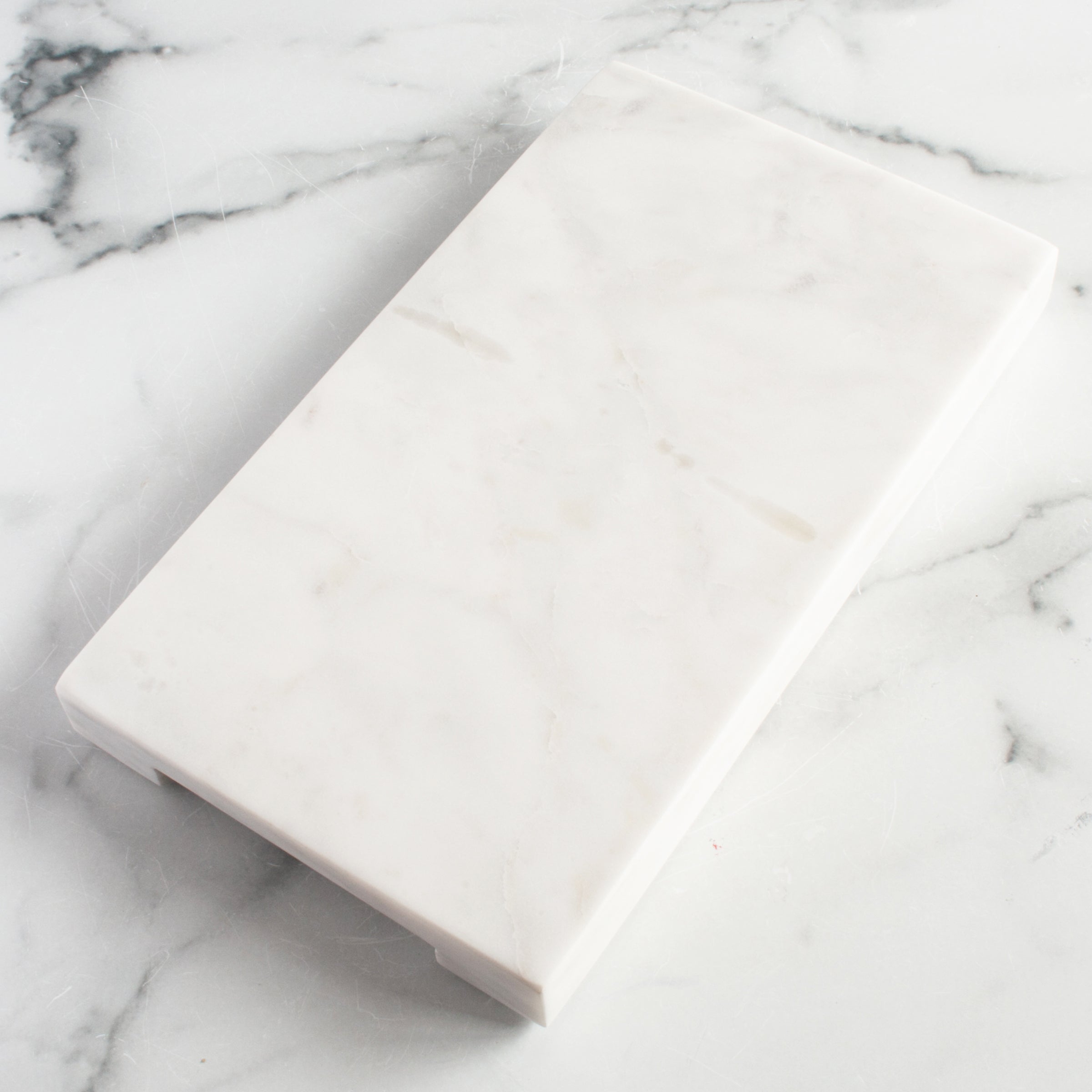 https://igourmet.com/cdn/shop/products/13729_be_home_white_marble_thick_rectangular_board_with_handle_grooves.jpg?v=1675570072